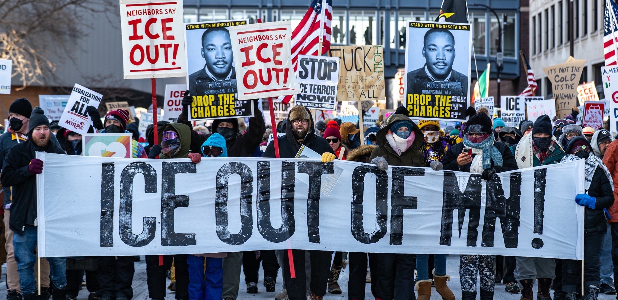 A big crowd carries a banner “ICE out of MN!”