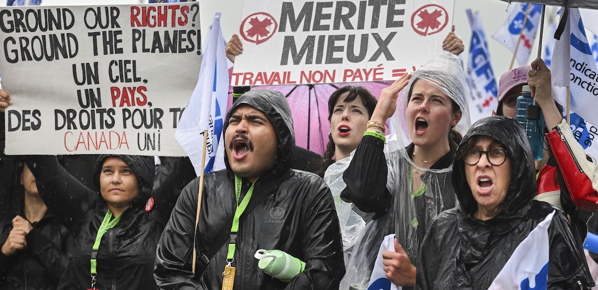 Six picketers hold signs in the rain, including, “Ground our rights? Ground the planes!”