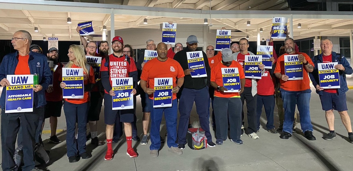 Workers in red shirts stand in a row with UAW signs