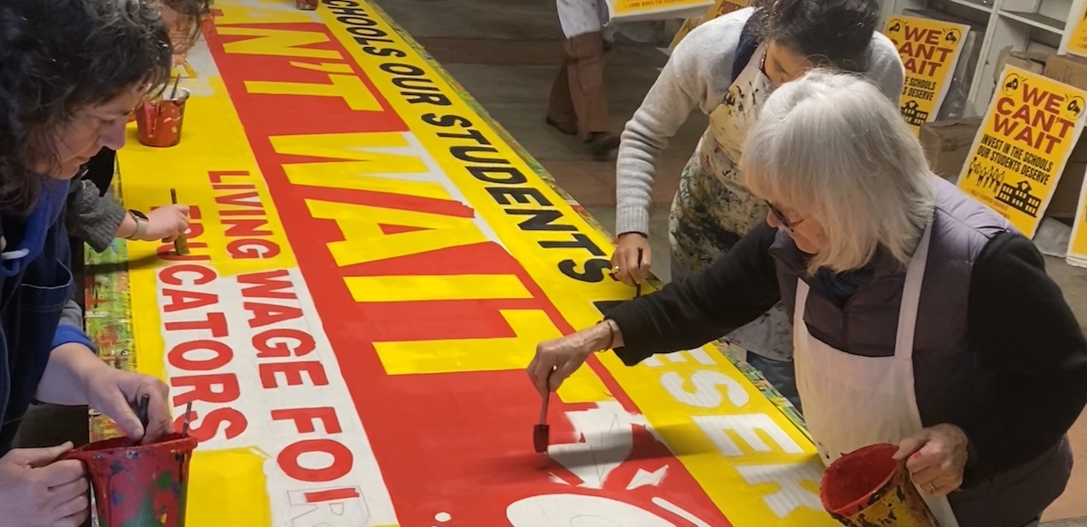Several people paint a big banner that says ‘We Can’t Wait.’