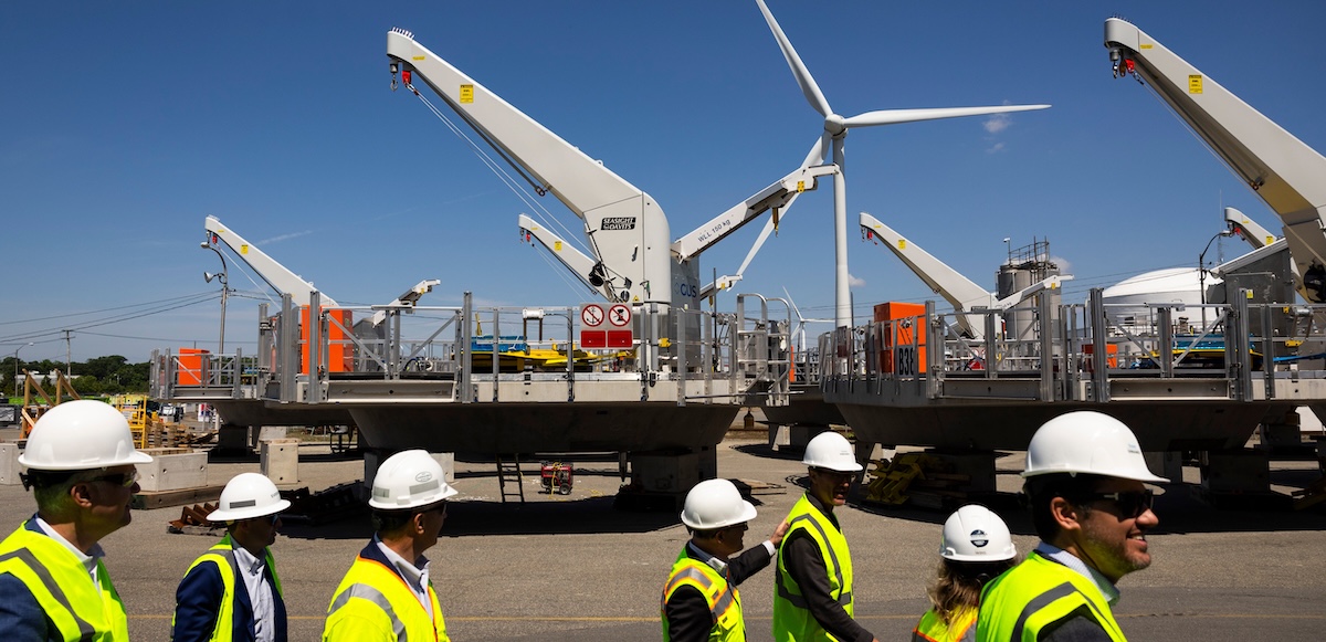 A group of people in hi-viz vests and hardhats walk by huge turbine components