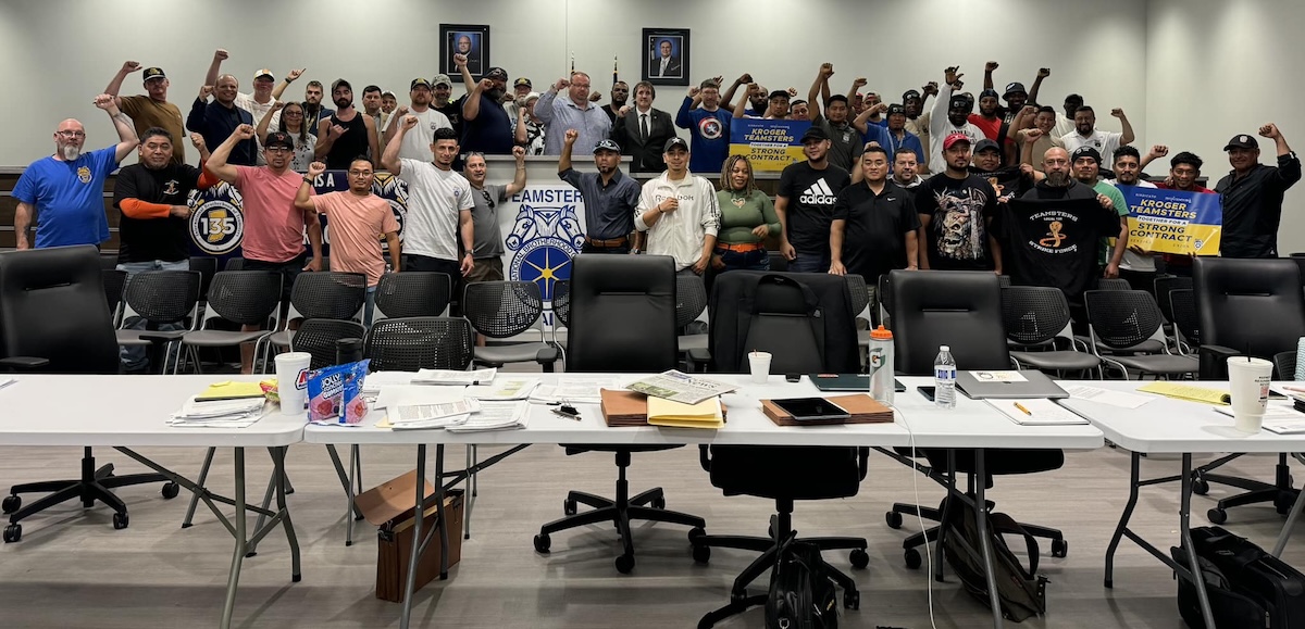 A group of 50 people stand behind a bargaining table with fists raised.