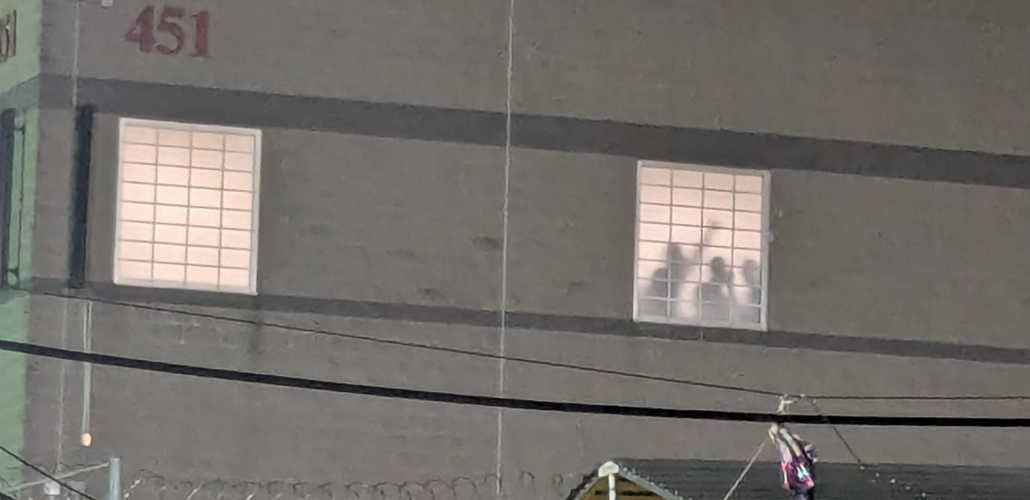 A photo taken at night shows detainees silhouetted in the prison window, one with fist raised.