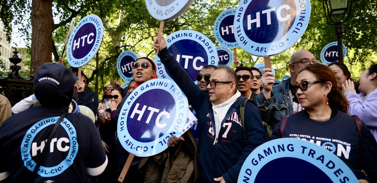 Several people chant with round Hotel Trades Council signs.