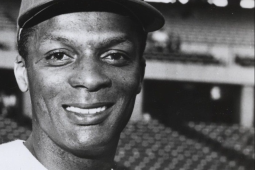 Center fielder Curt Flood smiles in a close-up head shot with stadium seating behind him.