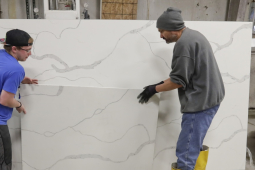 Two workers place a slab of manufactured stone against a larger slab.