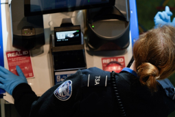 A TSA worker, seen over her shoulder, motions a passenger forward with a blue gloved finger