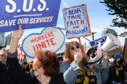 A close crowd with signs, including ‘Save our Services’ and someone with a bullhorn