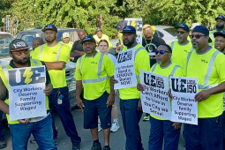 A group of Black men in hi viz green shirts hold signs saying “City workers demand family supporting wages”