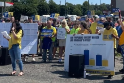 A group of 50 in yellow union shirts rallies in a grocery store parking lot.