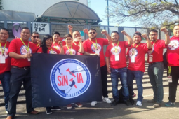 Members of SINTTIA's salary revision committee pose in red union shirts with fists raised up in the air in front of the Federal Center for Conciliation and Labor Registration.