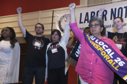 Several people stand on stage with fists raised and with a Labor Notes banner behind them.