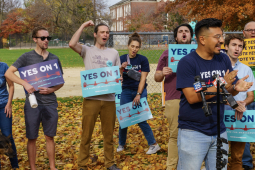 A group of excited people hold blue signs saying “Yes on 1”