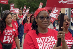 A group of nurses in red T-shirts with signs walk towards the camera.