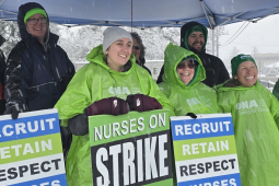 Six smiling people with green and blue strike signs stand under a tent in the snow.