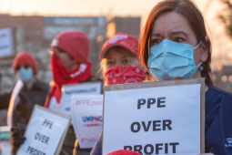 Masked workers in University of Michigan RN stand outside at dusk or dawn carrying home-printed signs: "PPE OVER PROFIT"