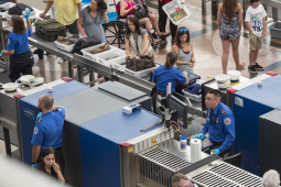 TSA workers are shown screening bags and scanning passengers at an airport