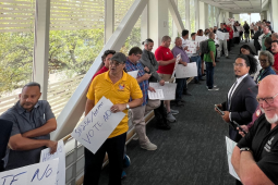 People in different colored union shirts or suits line both sides of a glass hallway. Many are men, some are Black and some are white. A few carry handmade signs urging a no vote on HB 1445.