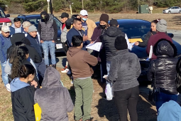 A group of workers stand by the side of the road while and man and woman pass out information to them.