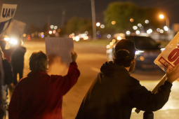 Workers hold signs at night--they are backlit by traffic and street lights but one sign is legible, saying ‘everyone tier one.’