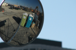 Two portajohns are reflected in a truck side mirror.