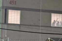 A photo taken at night shows detainees silhouetted in the prison window, one with fist raised. 
