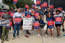 A group of workers pose for the camera on a city sidewalk. They are diverse in race, gender, and age. Many hold printed red and blue signs that say "PECO workers on strike!" One holds a big hand-drawn sign: "26+666+614=1. IBEW united!"