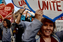 Protesters crowd towards the camera with heart-shaped signs saying “workers unite” and “hands off our postal service”