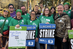 A group of green-shirted union members hold strike signs and smile.