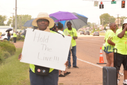 A woman holds a sign reading Hold the Line while others stand on the picket line.