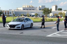 Workers outside a big plant approach a car with leaflets.
