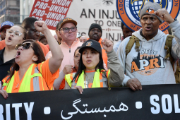 Members of the Laborers Union march during the May Day rally in New York City, behind a black banner that says solidarity in multiple languages, including Arabic.