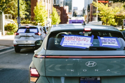 A car back window carries signs, including one saying, “Would you drive 10 miles for $4? Raise the Pay!”