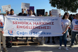 A group of 30 men and women with signs in Turkish stand outside behind a banner