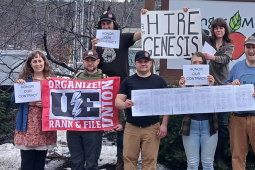 Eight people outside face the camera with signs, including “Hire Genesis” and a UE banner. 