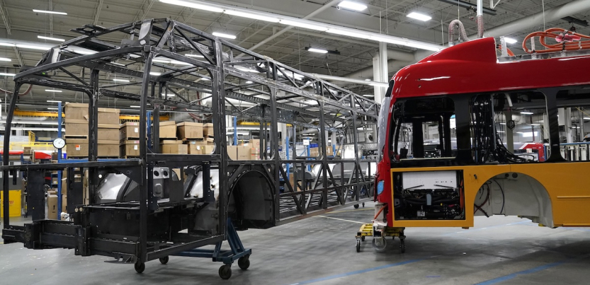 The skeleton of an unfinished bus, and the outer shell of another are shown in a factory