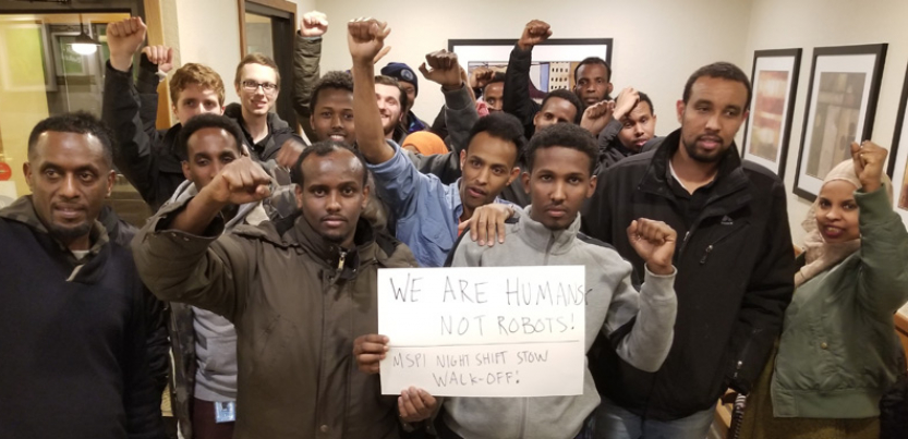 Amazon workers with fists raised gathered around a sign.
