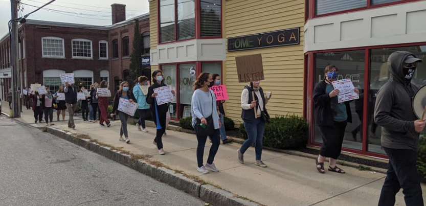 A group of teachers marches on the sidewalk in downtown Andover, Massachusetts.