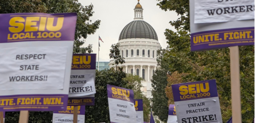 Printed SEIU Local 1000 picket signs reading "Respect state workers!!" and "Unfair practice strike!" are raised aloft with a capitol rotunda visible behind them.