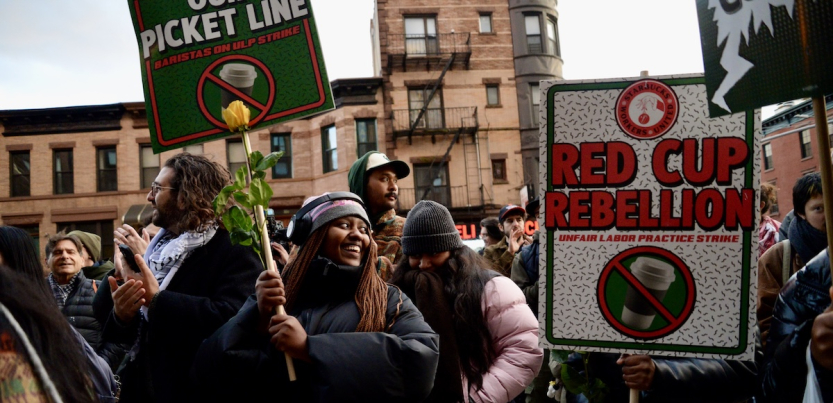 A group rallies holding signs that say Red Cup Rebellion: Unfair Labor Practice Strike, with a Starbucks coffee cup with a red line through it.