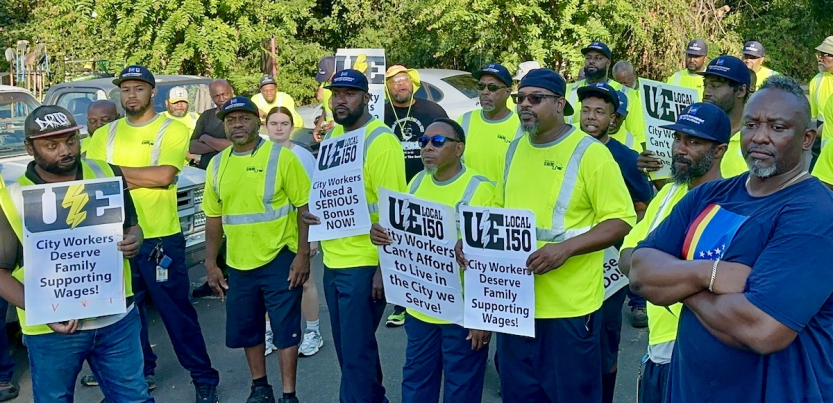 A group of Black men in hi viz green shirts hold signs saying “City workers demand family supporting wages”