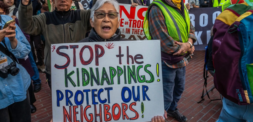 A woman holds a sign at a rally that reads Stop the Kidnappings! Protect Our Neighbors!