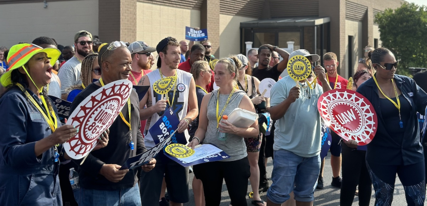 A crowd with UAW signs gathers outside a union hall for a rally.