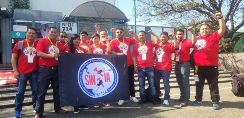 Members of SINTTIA's salary revision committee pose in red union shirts with fists raised up in the air in front of the Federal Center for Conciliation and Labor Registration.