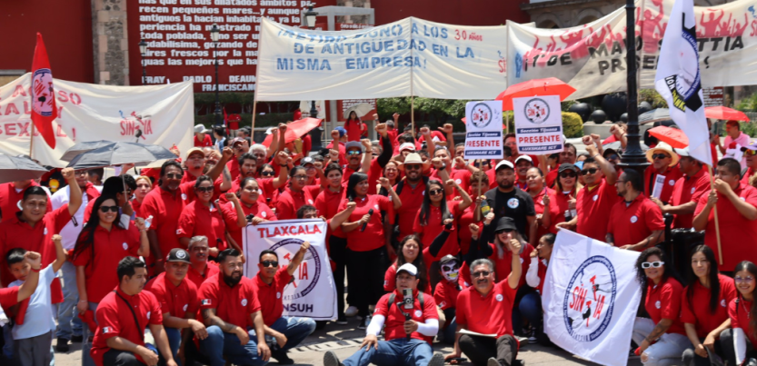 A large crowd of SINTTIA members in red shirts hold banners celebrating May Day