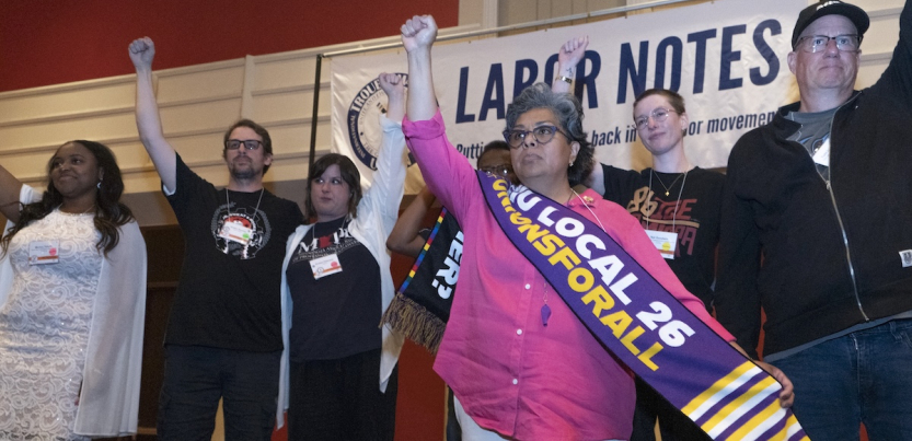 Several people stand on stage with fists raised and with a Labor Notes banner behind them.