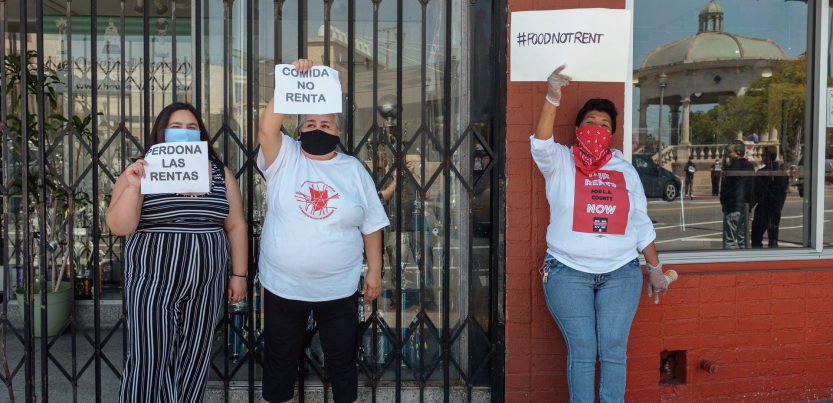 Three women hold signs saying "Food Not Rent" and "Cancel Rent" in English and Spanish.