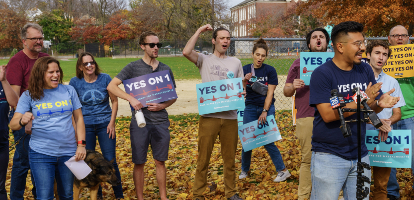 A group of excited people hold blue signs saying “Yes on 1”