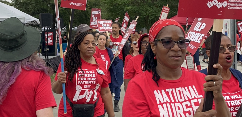 A group of nurses in red T-shirts with signs walk towards the camera.
