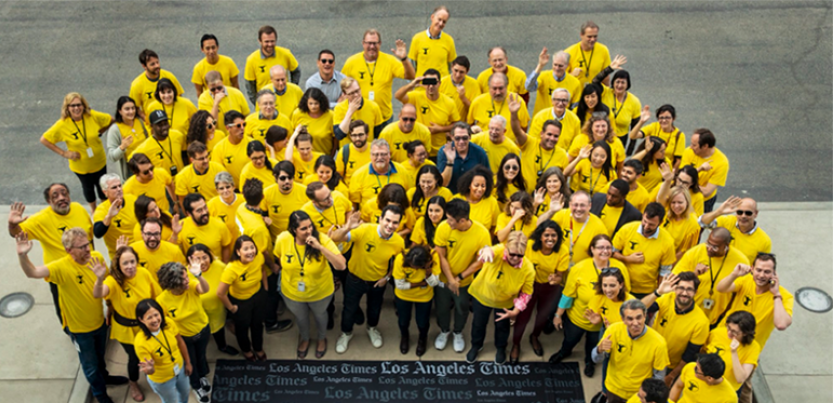 L.A. Times employees gather as NewsGuild members wearing bright yellow shirts around a plaque that says LA Times.